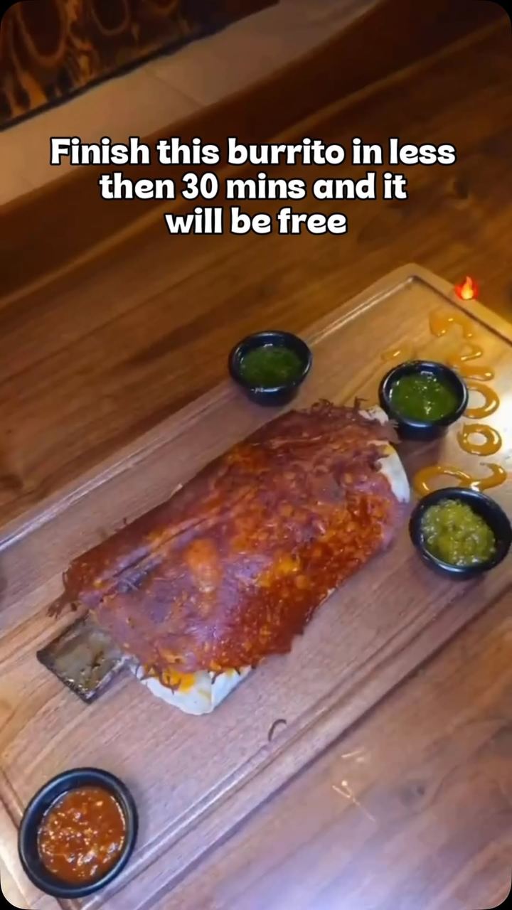 The Texas Dinorito Burrito on a wooden board with dipping sauces, captioned: finish this burrito in less than 30 minutes and it will be free